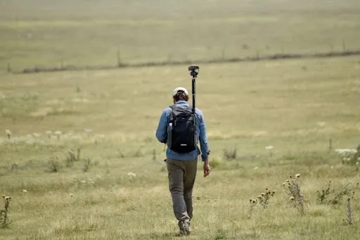 Kelly Goff walking away across open Colorado grassland with a GNSS receiver on a pole strapped to his backpack