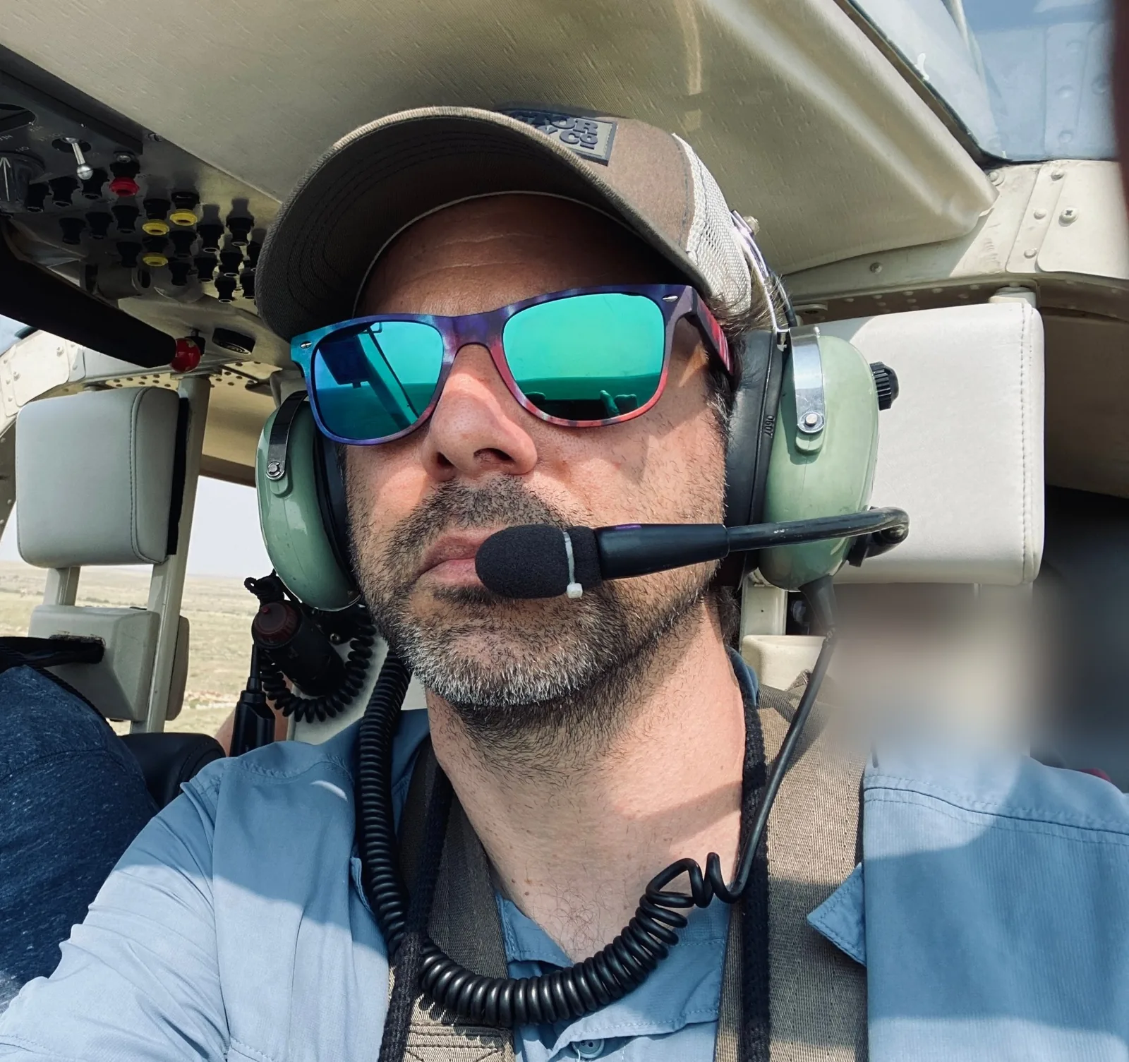The artist in a helicopter cockpit wearing a headset and sunglasses