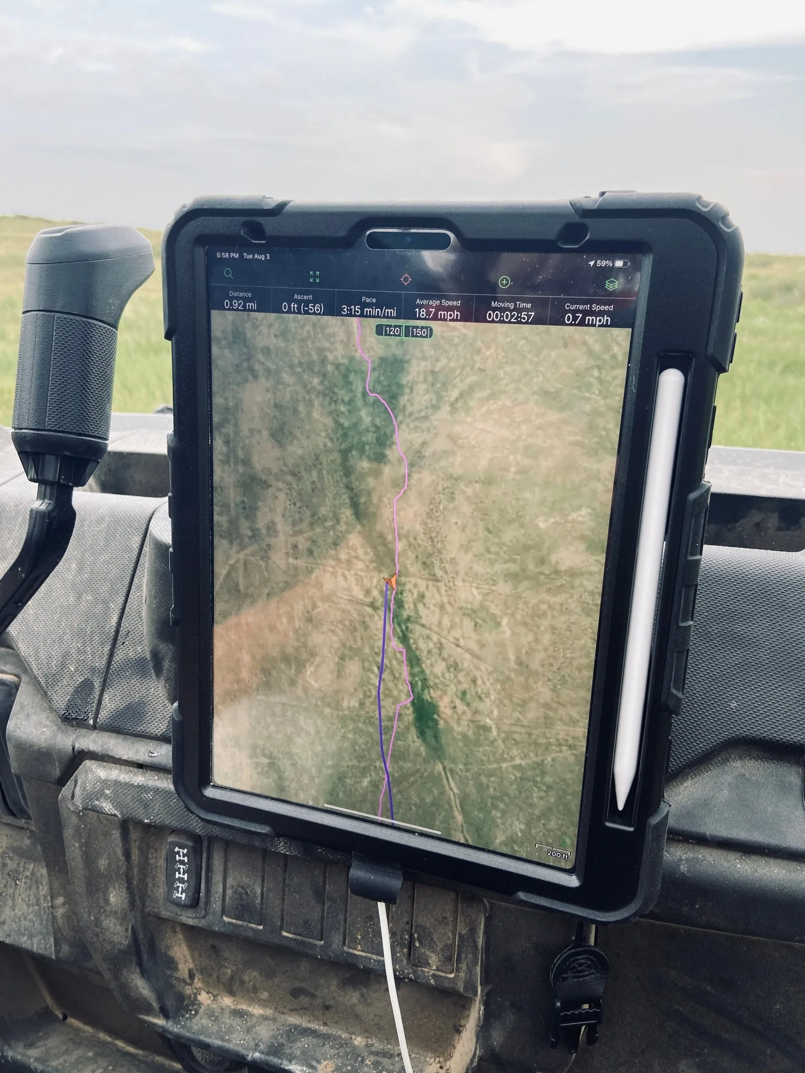 A tablet on an ATV dashboard showing a pink track and a blue route line on a satellite map